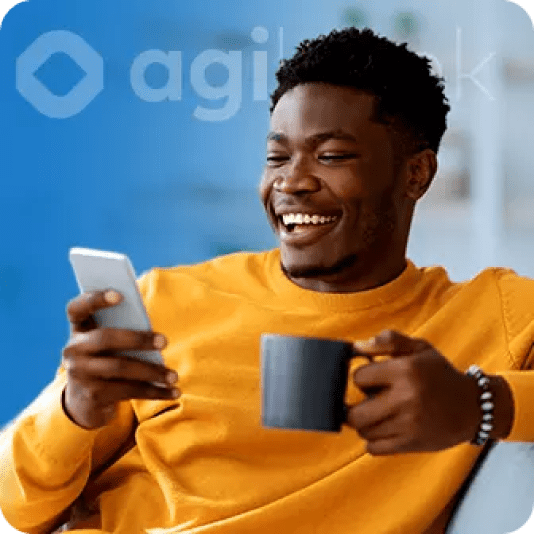 uma homem sorrindo olhando o celular e com uma caneca na mão