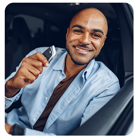 Homem sorrindo dentro de um carro, segurando a chave do veículo na mão.