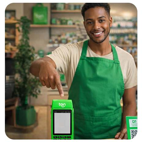 Homem sorrindo com avental verde apontando para maquininha de pagamento Ton em ambiente comercial.