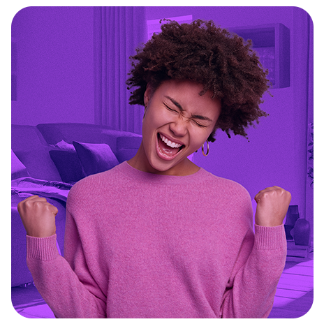 Mulher comemorando com expressão de alegria, punhos cerrados, em ambiente interno com fundo roxo.