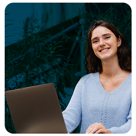 Mulher sorrindo usando notebook em ambiente com plantas ao fundo.