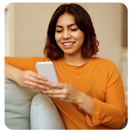 Mulher sorrindo enquanto usa o celular sentada no sofá.