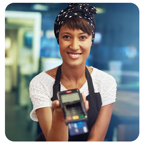 Mulher jovem, negra, sorrindo, com um lenço na cabeça, segurando uma maquininha de cartão.