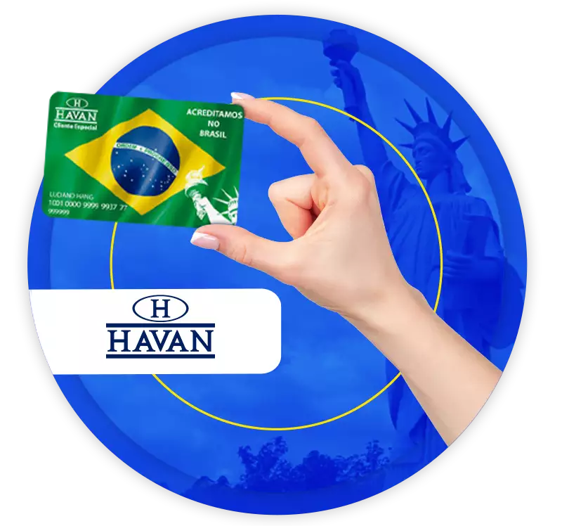 uma mão feminina segurando um cartão da Havan, com a bandeira do Brasil impressa nele, tendo ao fundo a Estátua da Liberdade da Havan