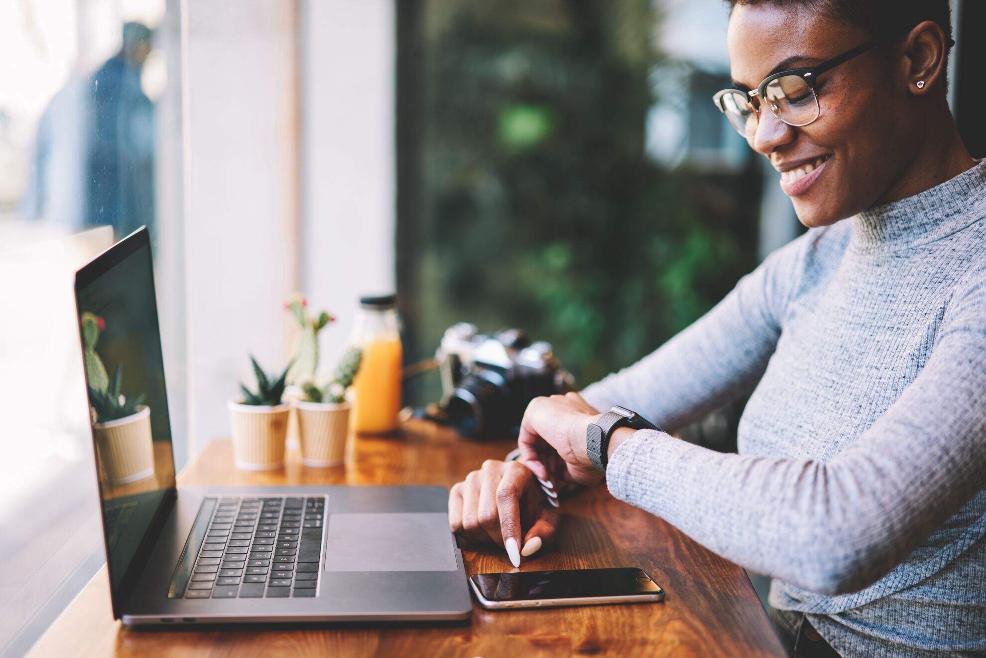 Moça negra mexendo no celular, com o notebook aberto na sua frente