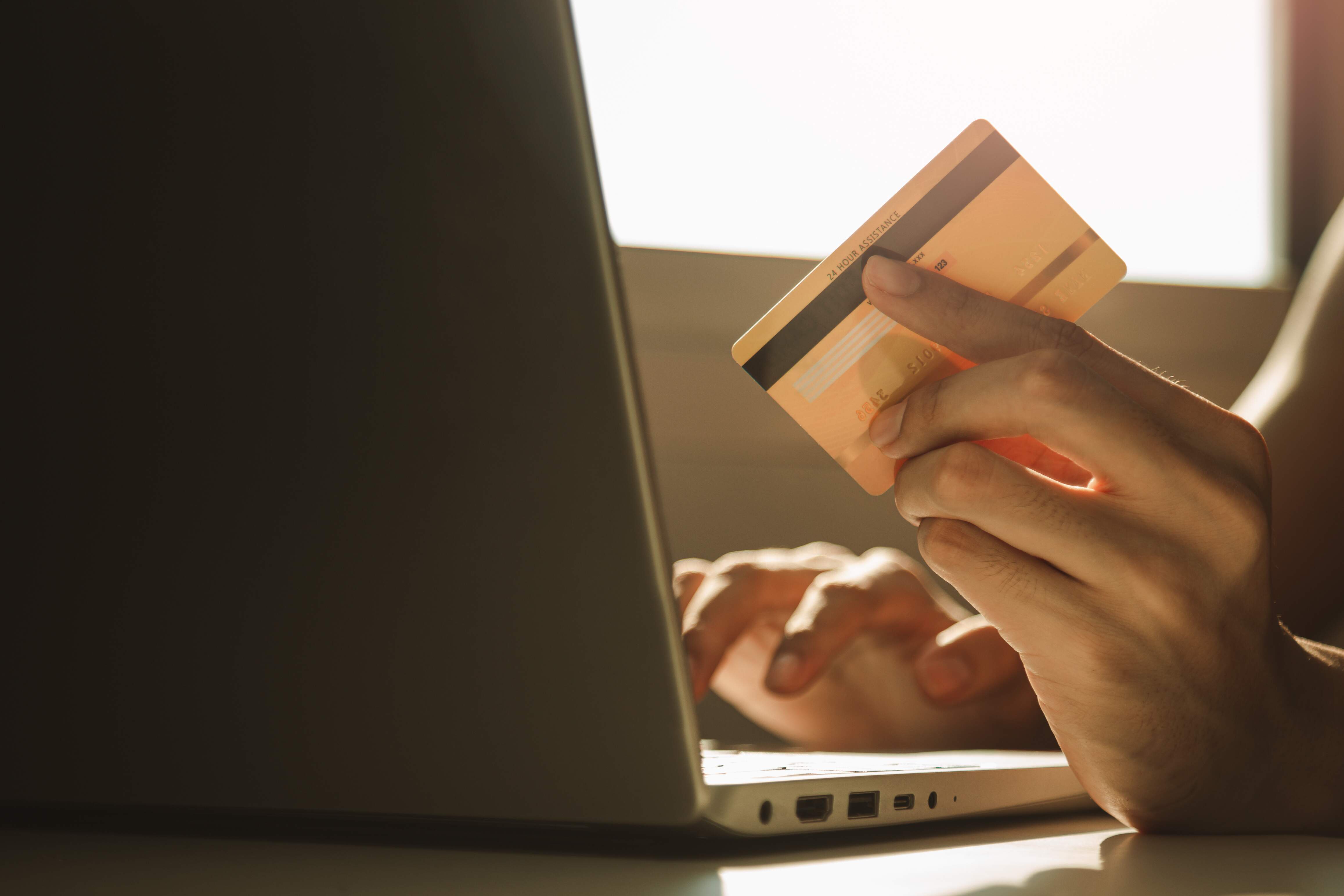 Uma pessoa usando o computador segurando um cartão para negociar dívida Banco Pan