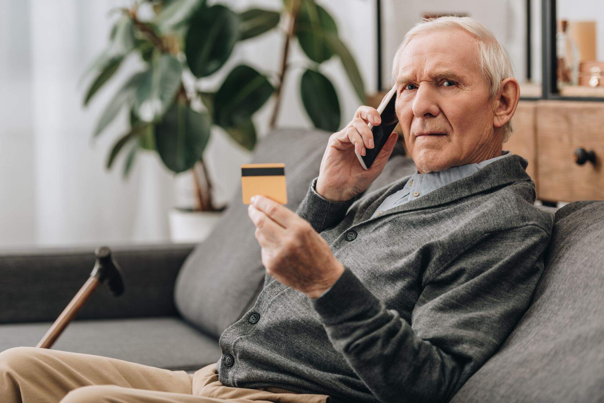 Homem idoso segurando o seu cartão de crédito e falando ao telefone